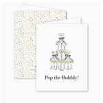 Front and back of a folded greeting card featuring an illustration of a champagne tower with black bows and the text “Pop the Bubbly!” on the front; blank inside with a gold confetti-style back pattern and includes a Euro flap envelope.