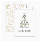 Front and back of a folded greeting card featuring an illustration of a champagne tower with black bows and the text “Pop the Bubbly!” on the front; blank inside with a gold confetti-style back pattern and includes a Euro flap envelope.