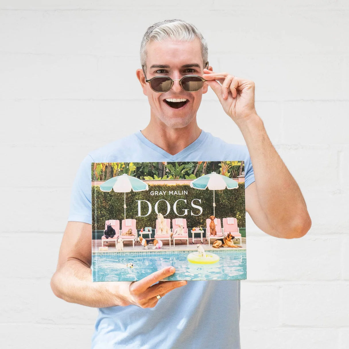 Man holding a book titled 'DOGS' by Gray Malin against a white background
