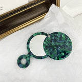 Green marbled hand mirror on a white surface with a wooden frame in the background