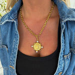 Person wearing a gold chain necklace with a pendant, and a denim jacket