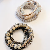 wo sets of multi-layered beaded bracelets, one with soft neutral stones and the other with black and speckled beige beads, displayed on a white background.