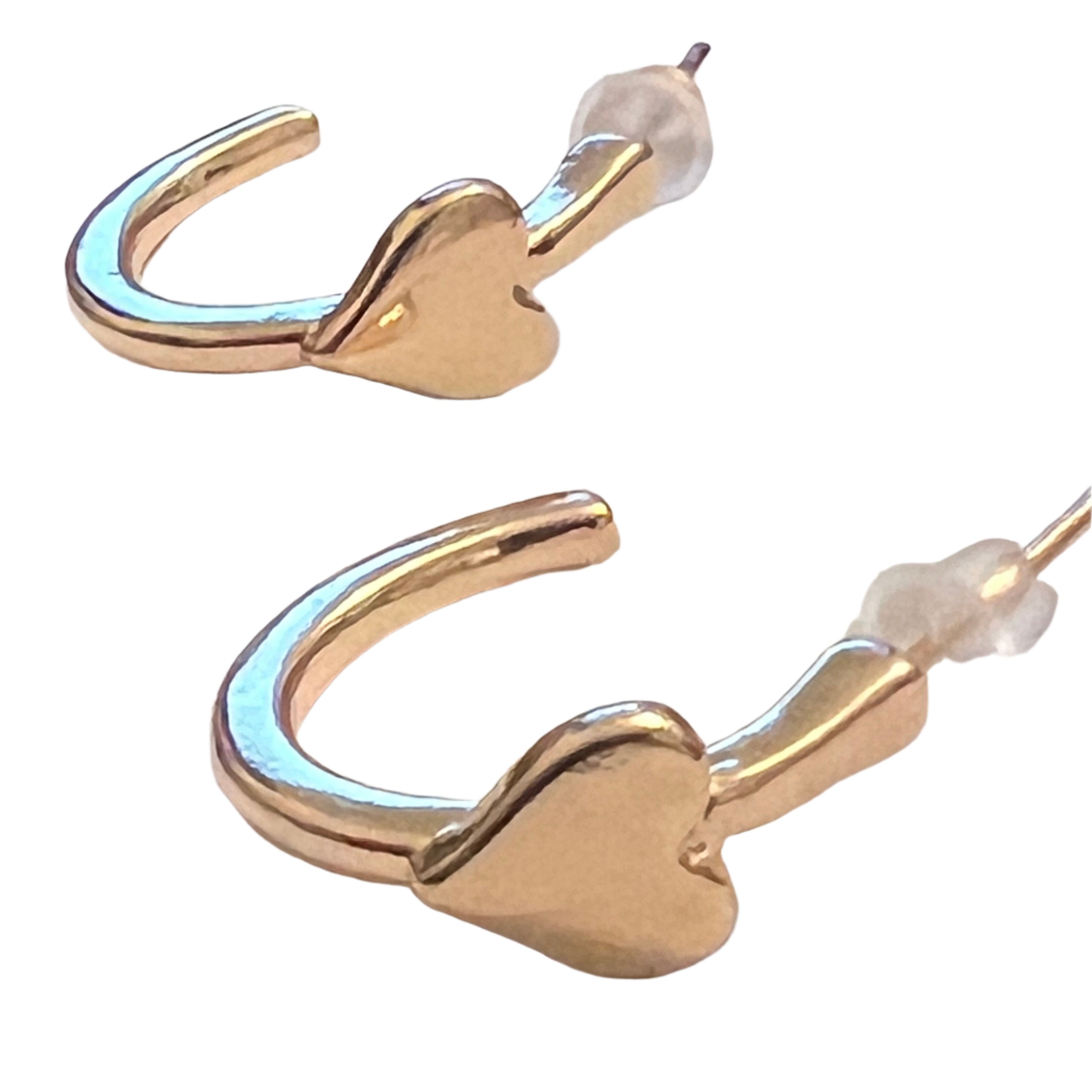 A pair of gold hoop earrings with integrated heart-shaped details and push-back closures, displayed on a white surface with a soft background.