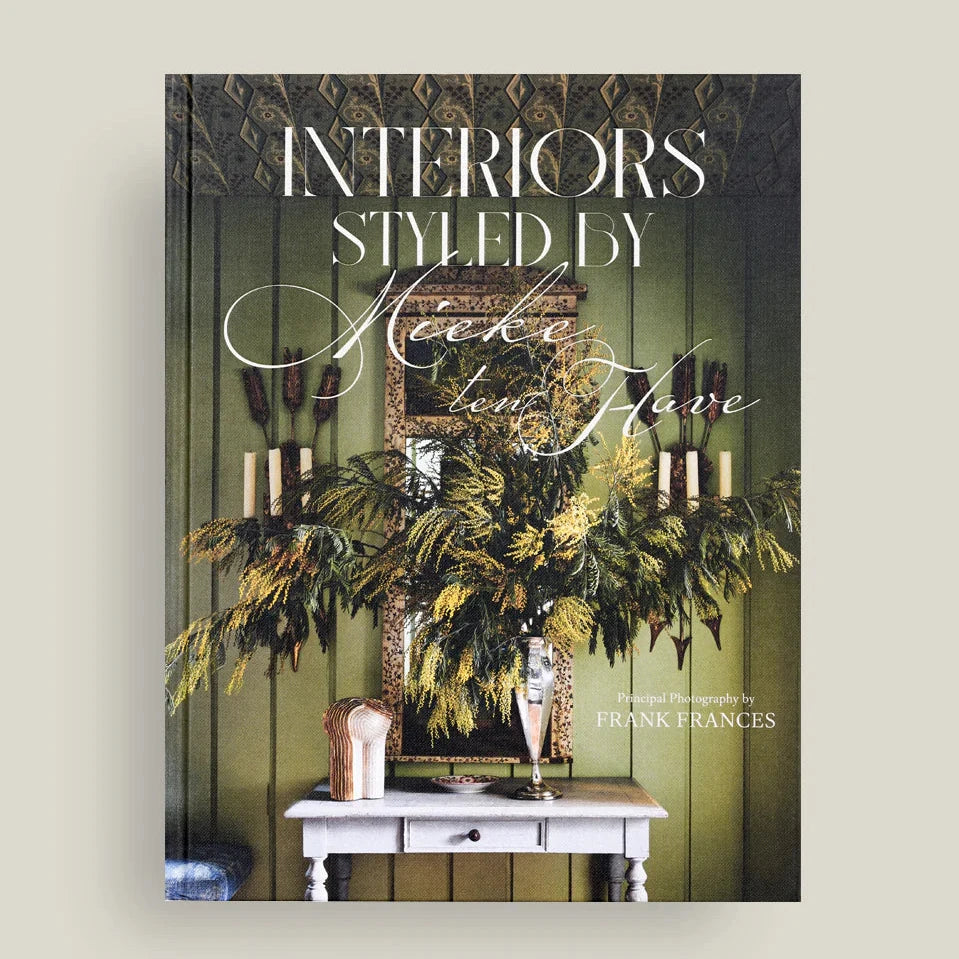 Book cover of 'Interiors Styled by' with decorative elements on a green wall.