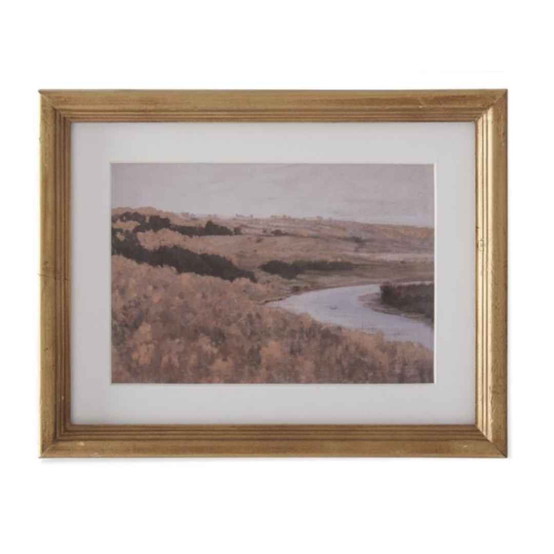Framed landscape print of a river and trees with a gold frame on a white background