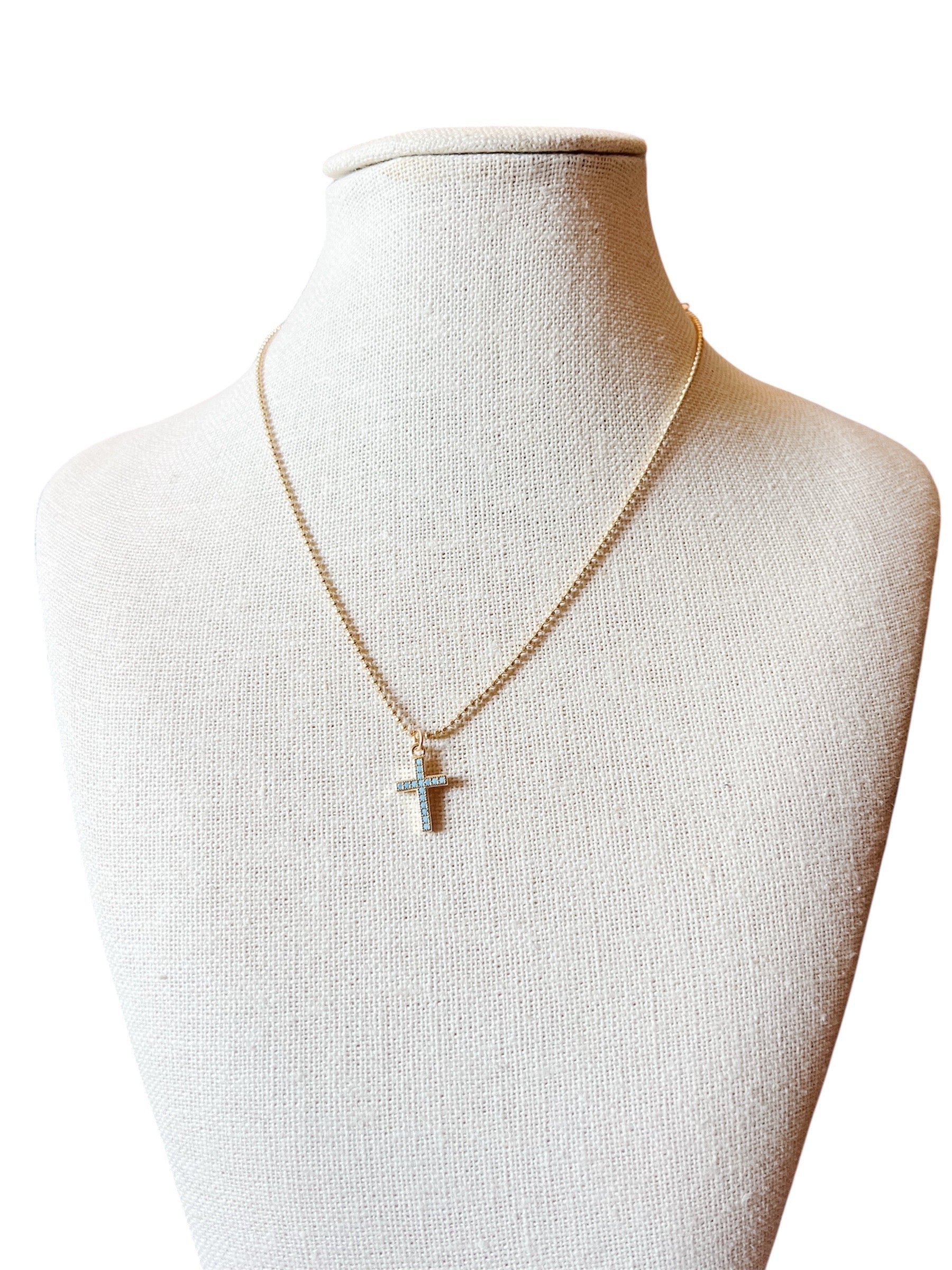  Liana Necklace features a gold beaded chain and a cross charm accented with subtle blue details. 