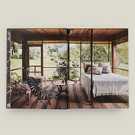 Bedroom with a view of a garden through large windows, featuring a bed, chairs, and a table.