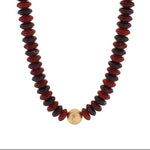 Necklace with red and black beads and a gold charm on a white background