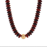 Necklace with red and black beads and a gold charm on a white background
