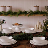 Christmas-themed table setting with white dishes, greenery, and decorative items on a wooden shelf.