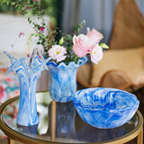 Blue glass vase, bowl, and flower arrangement on a table with blurred background