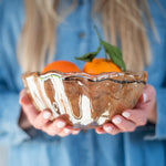 Person holding a glass bowl with mandarins against a blurred blue background