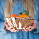 Person holding a glass bowl with mandarins against a blurred blue background