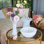 Decorative table setting with flowers and a bowl on a glass table.
