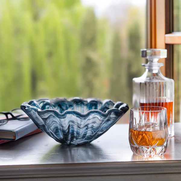 Onda fluted Glass bowl, glass with liquid, and decanter on a surface with a blurred natural background