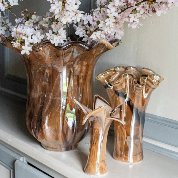 Set of three brown ceramic vases with floral arrangement on a shelf.
