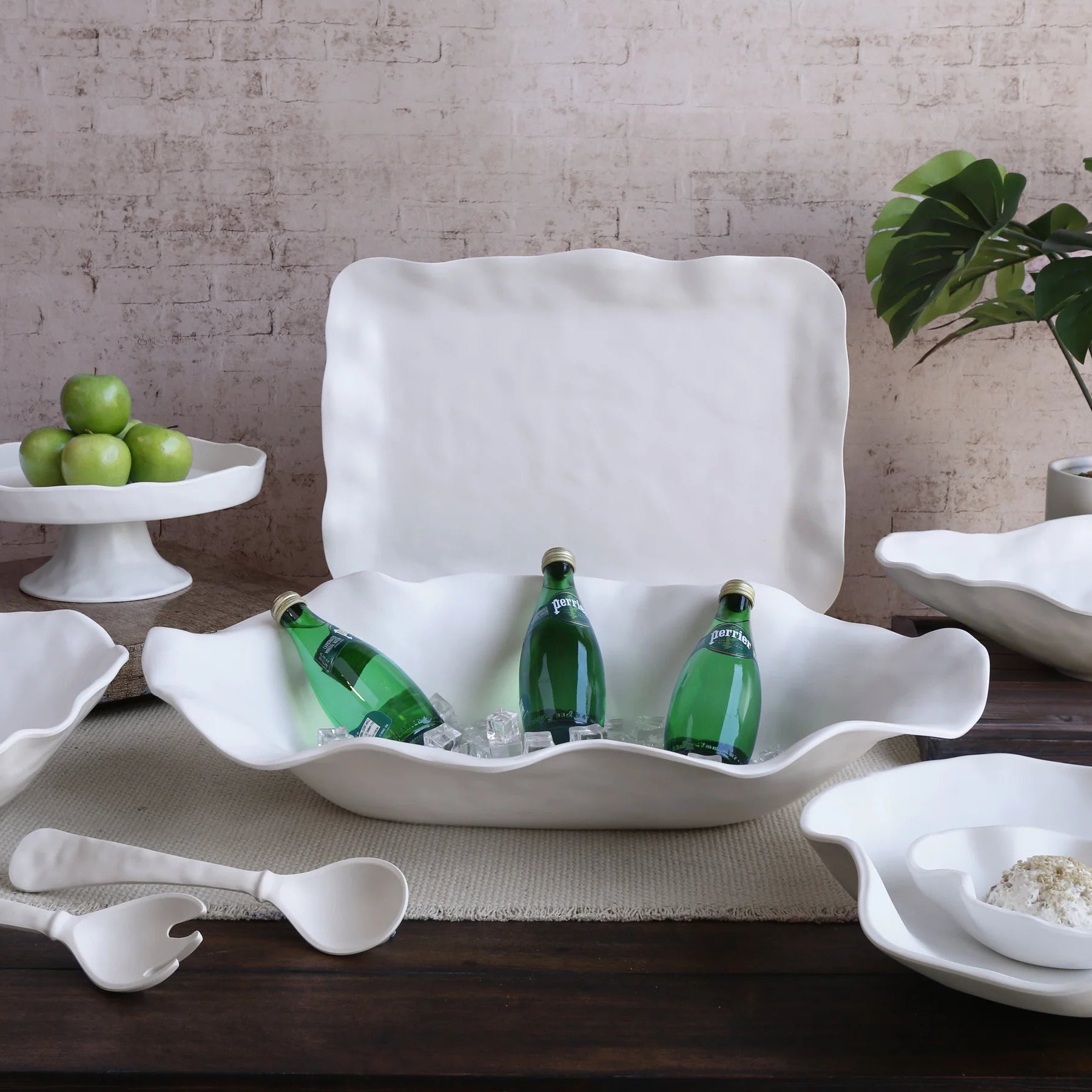 White shell-shaped ice bucket with green bottles on a wooden table with decorative items.
