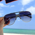 Sunglasses held up with a beach and blue sky in the background