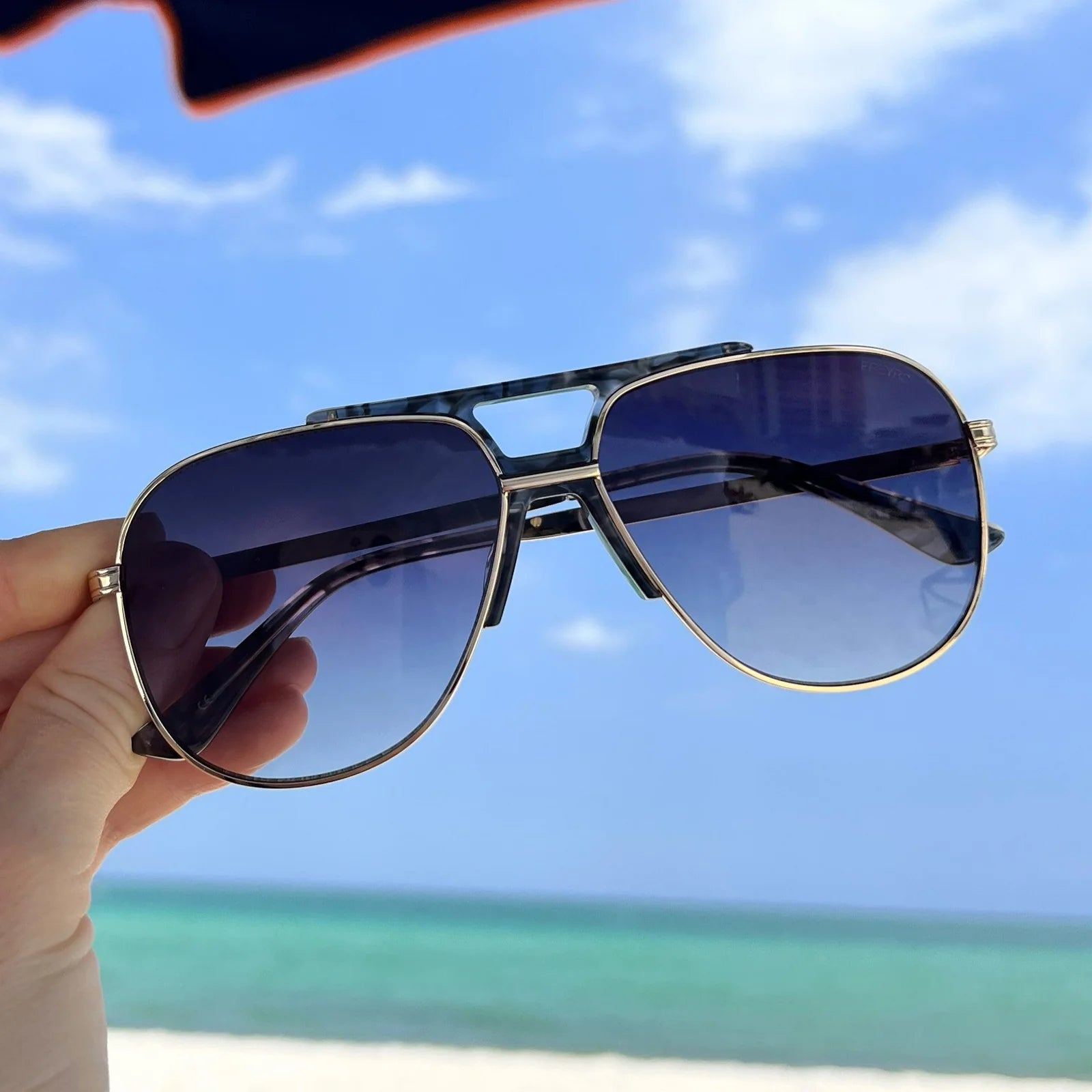 Sunglasses held up with a beach and blue sky in the background