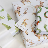 Roll of Christmas-themed wrapping paper with deer and wreath designs on a white background.