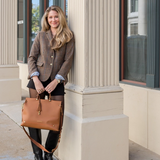 Woman holding a brown handbag standing against a building.