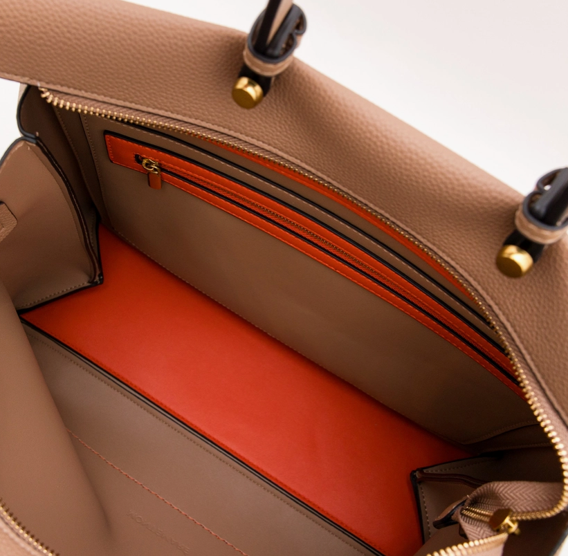 Close-up of a beige handbag with a red interior