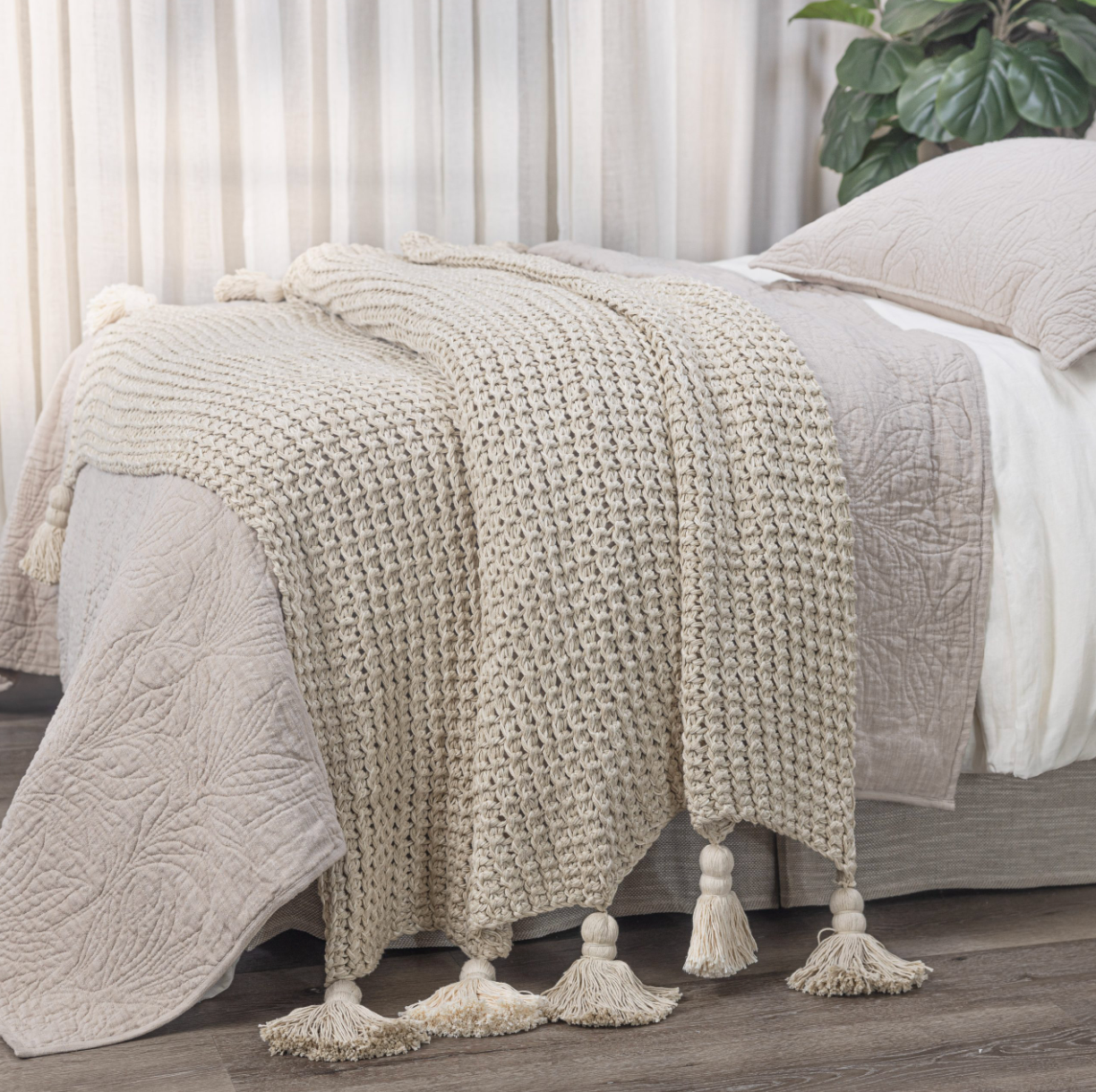 Beige knitted blanket with tassels on a bed in a bedroom setting