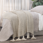 Beige knitted blanket with tassels on a bed in a bedroom setting