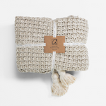 Beige woven blanket with tassels and a label on a white background