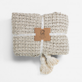 Beige woven blanket with tassels and a label on a white background