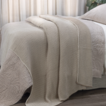 Textured beige blanket draped over a bed with a neutral background