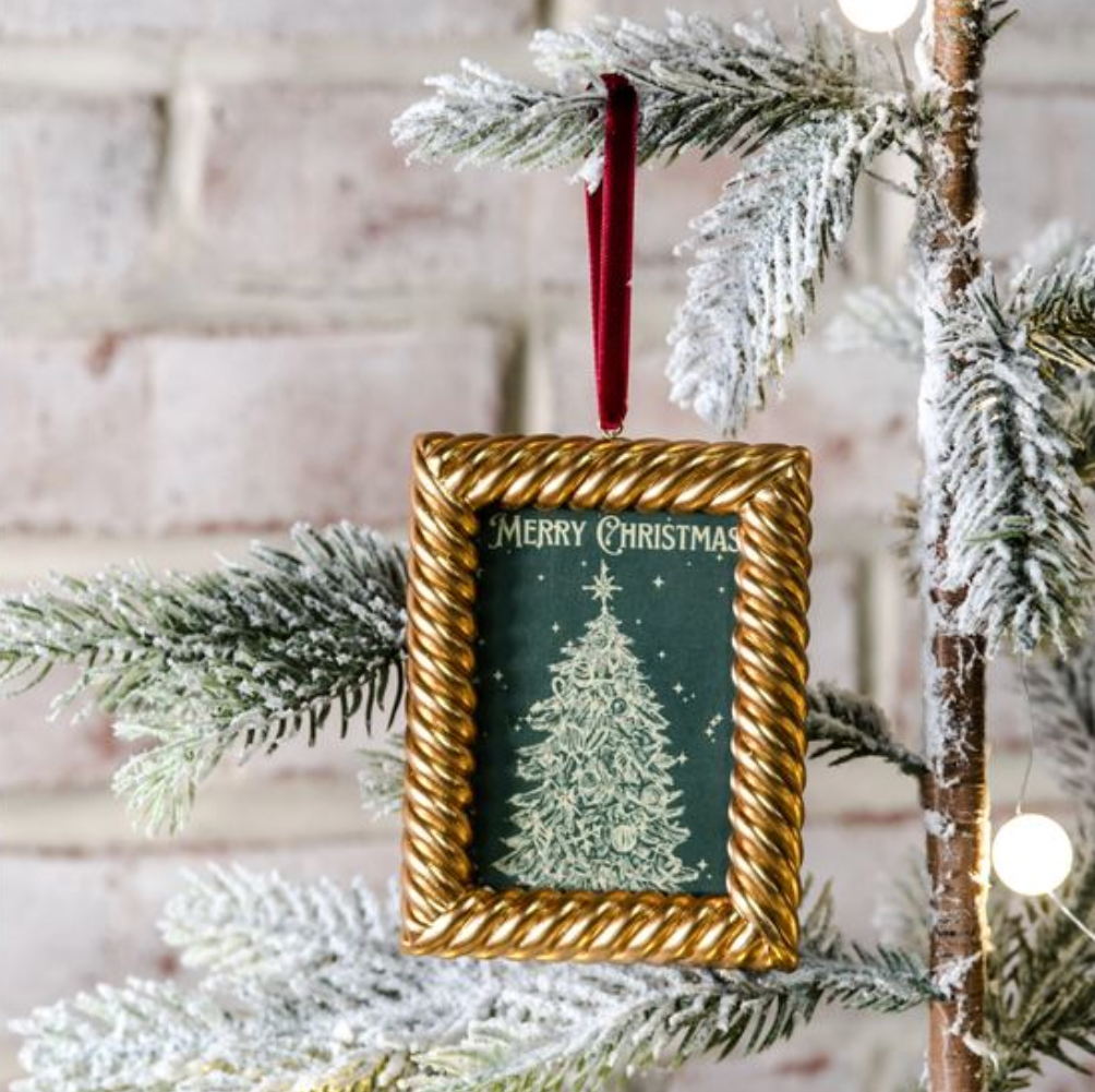 Decorative Christmas ornament with gold frame and 'Merry Christmas' text on a tree branch.