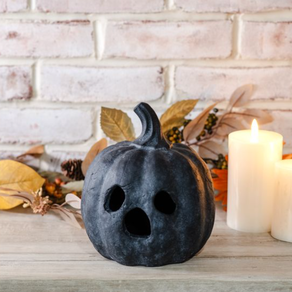 Decorative black pumpkin with carved facial features on a table with candles and autumn leaves.