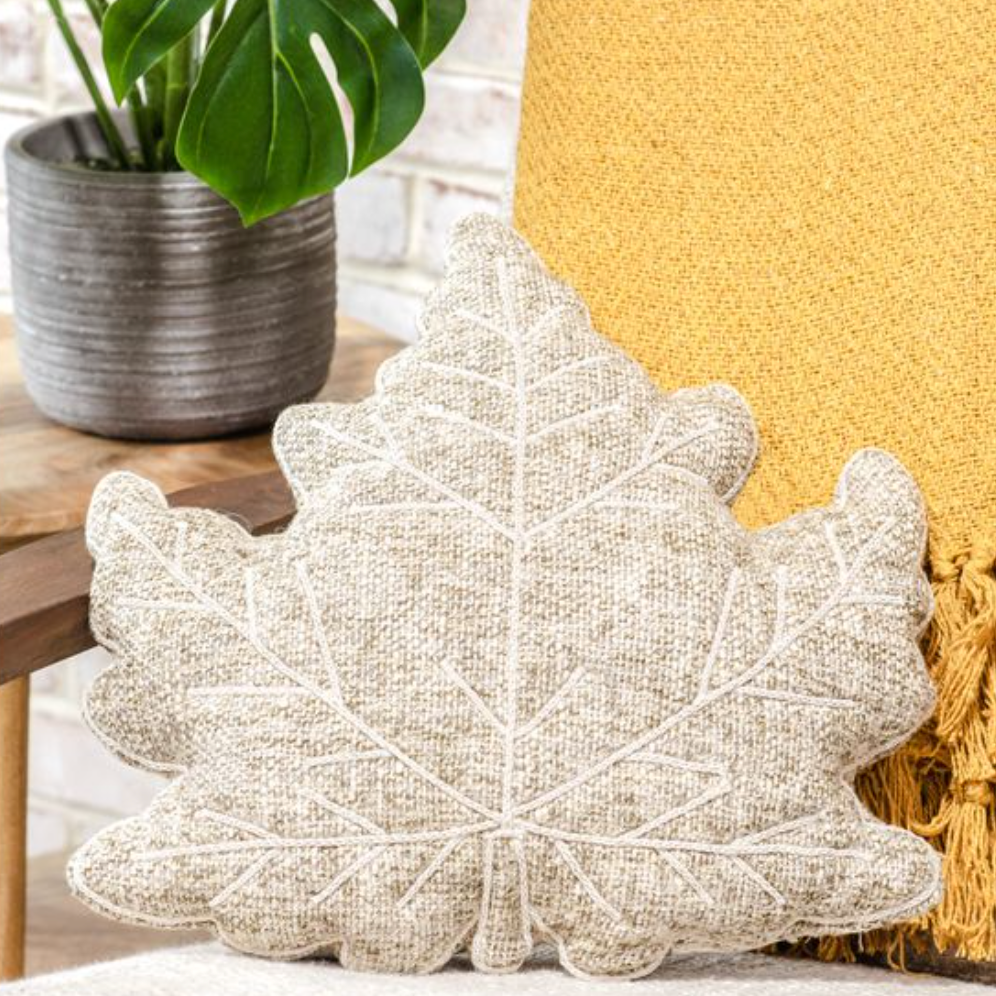 Leaf-shaped decorative pillow on a surface with a plant in the background