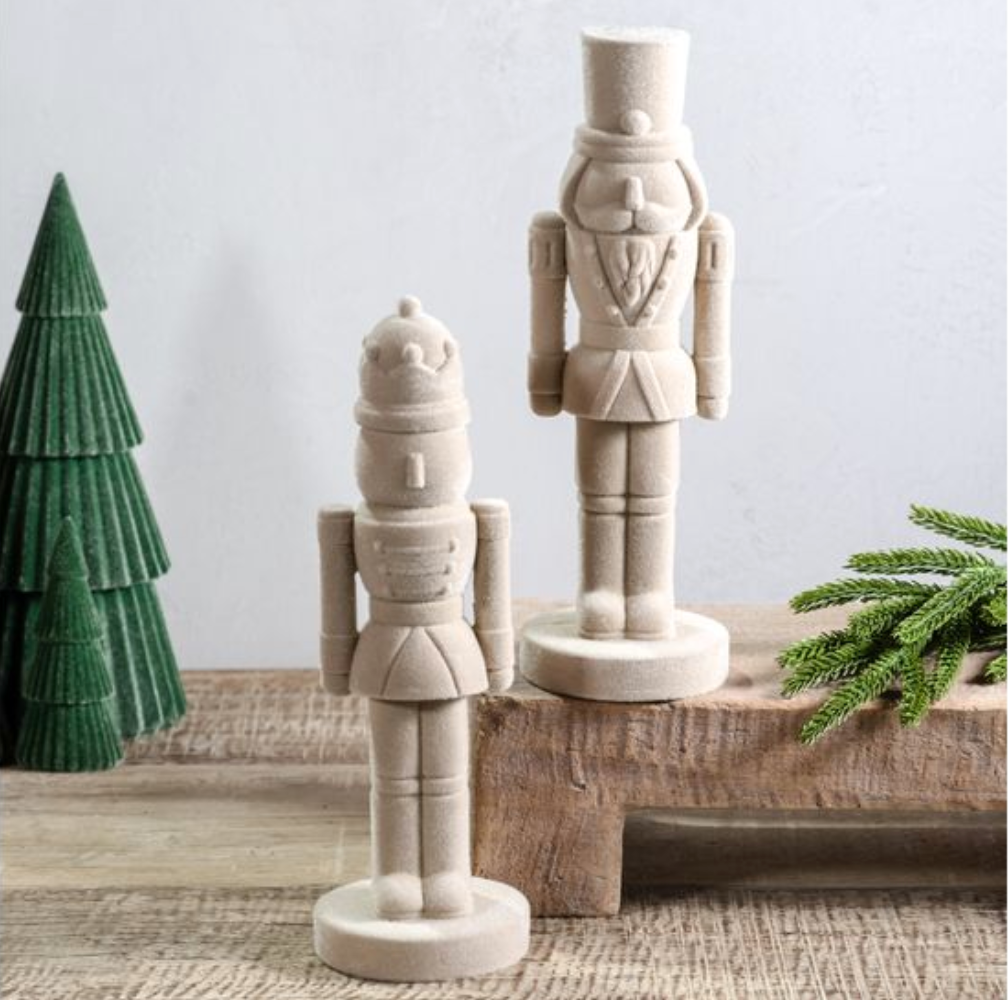 two velvet nutcrackers on a rustic surface with a green paper tree and greenery.