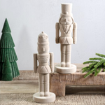 two velvet nutcrackers on a rustic surface with a green paper tree and greenery.