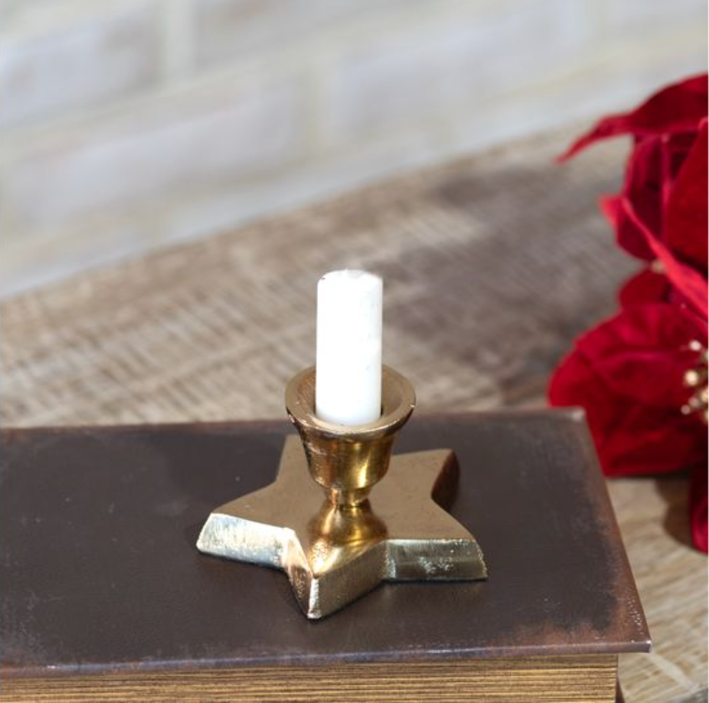 Gold candle holder with a white candle on an old book, with red flowers in the background.