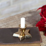Gold candle holder with a white candle on an old book, with red flowers in the background.