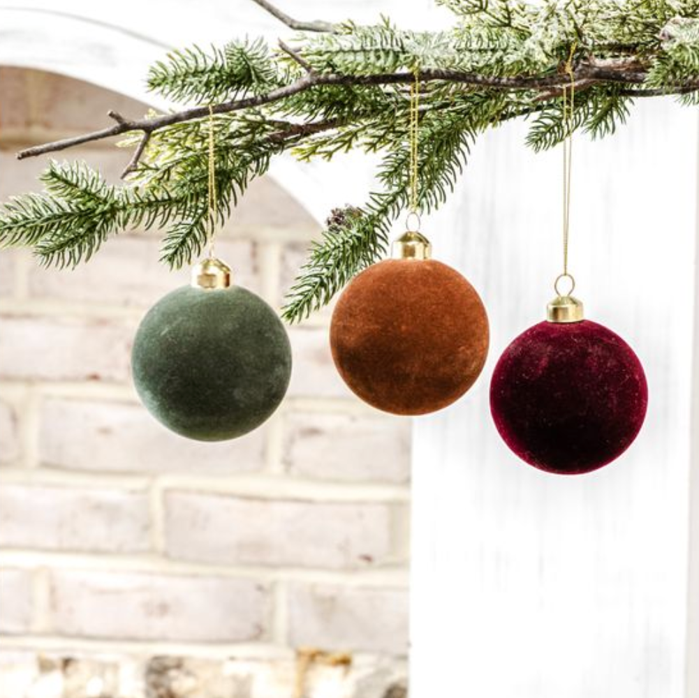 Three velvet Christmas ornaments in green, brown, and red hanging from a tree branch.