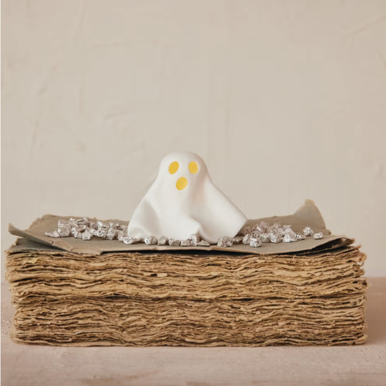 White ghost figurine on a stack of brown paper with a beige background