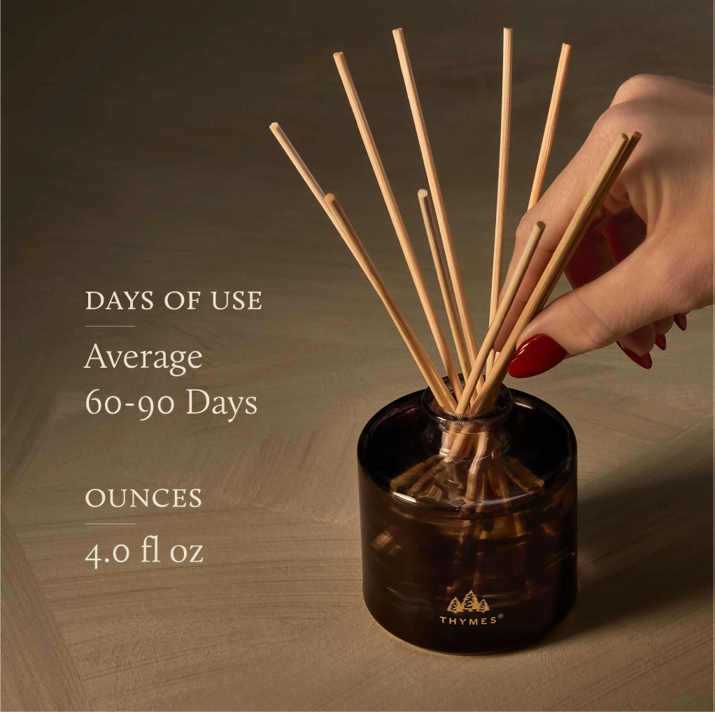 Hand holding a diffuser stick with product details on a wooden background