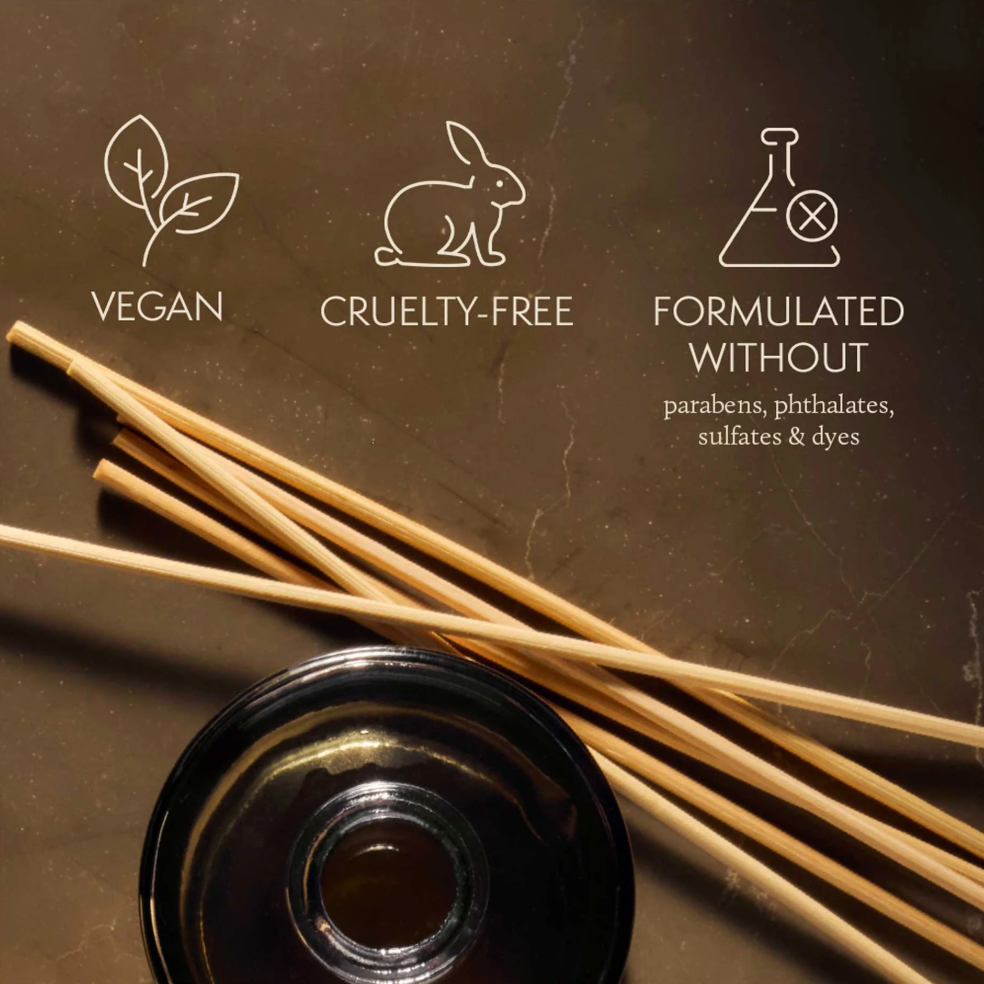 Reed diffuser with vegan, cruelty-free, and sulfate-free icons on a dark background