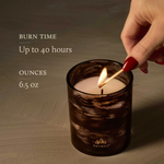 Candle being lit with text about burn time and ounces, on a wooden surface.