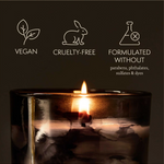 Candle in a glass holder with vegan, cruelty-free, and sulfate-free icons on a dark background.