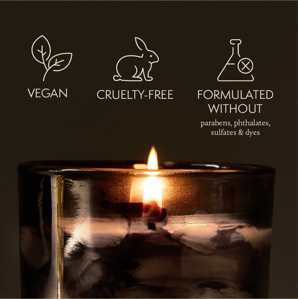 Candle in a glass holder with vegan, cruelty-free, and sulfate-free icons on a dark background.