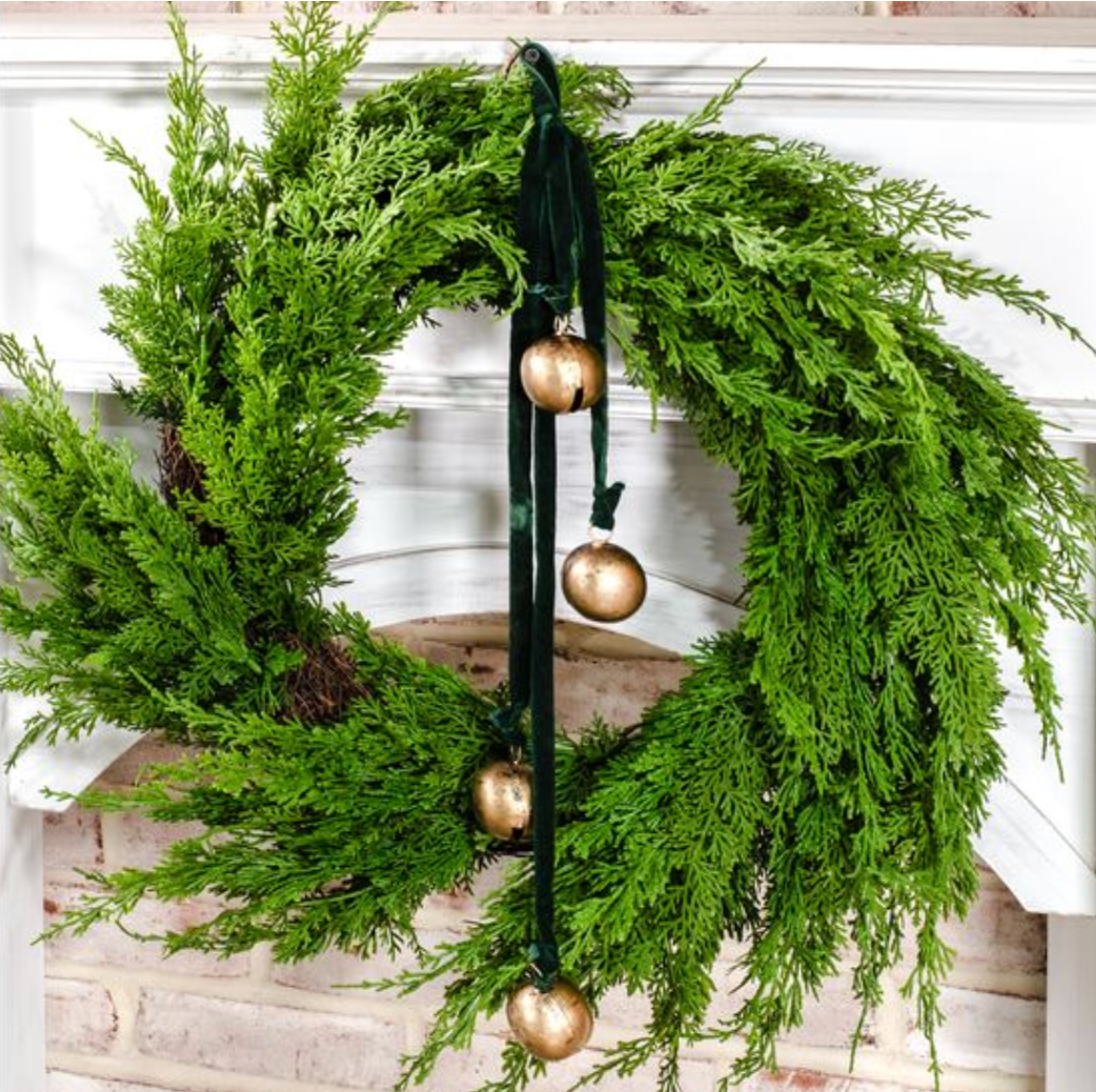 Green velvet wreath sash with gold bells on tied on green wreath on a white wall