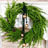 Green velvet wreath sash with gold bells on tied on green wreath on a white wall