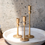 Three gold candle holders on a textured surface with a neutral background