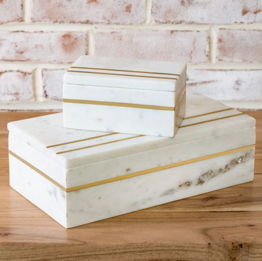 Marble boxes with gold stripes on a wooden surface with a brick wall background