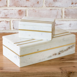Marble boxes with gold stripes on a wooden surface with a brick wall background